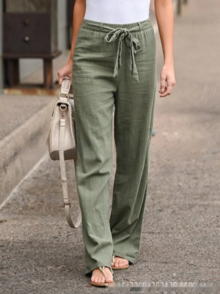 Woman wearing olive green drawstring linen pants and white top, holding beige handbag walking on street