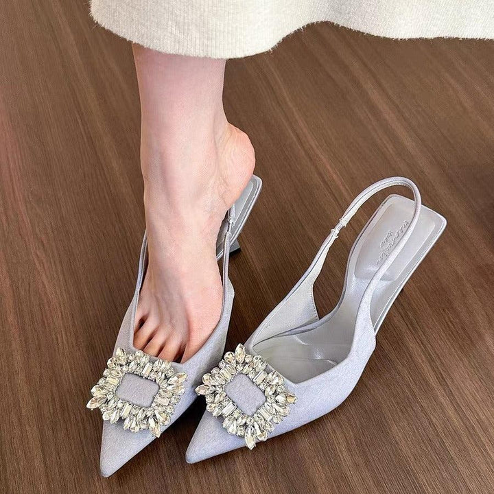 Woman wearing white pointed slingback heels with crystal embellishments on wood floor