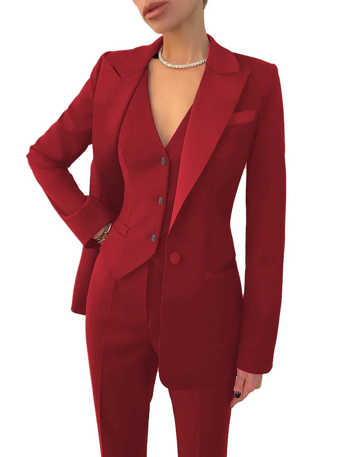 woman wearing a tailored red pantsuit with a blazer and vest, accessorized with a pearl necklace