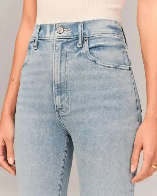 Close-up of light blue high-waisted denim jeans with button and front pockets on model