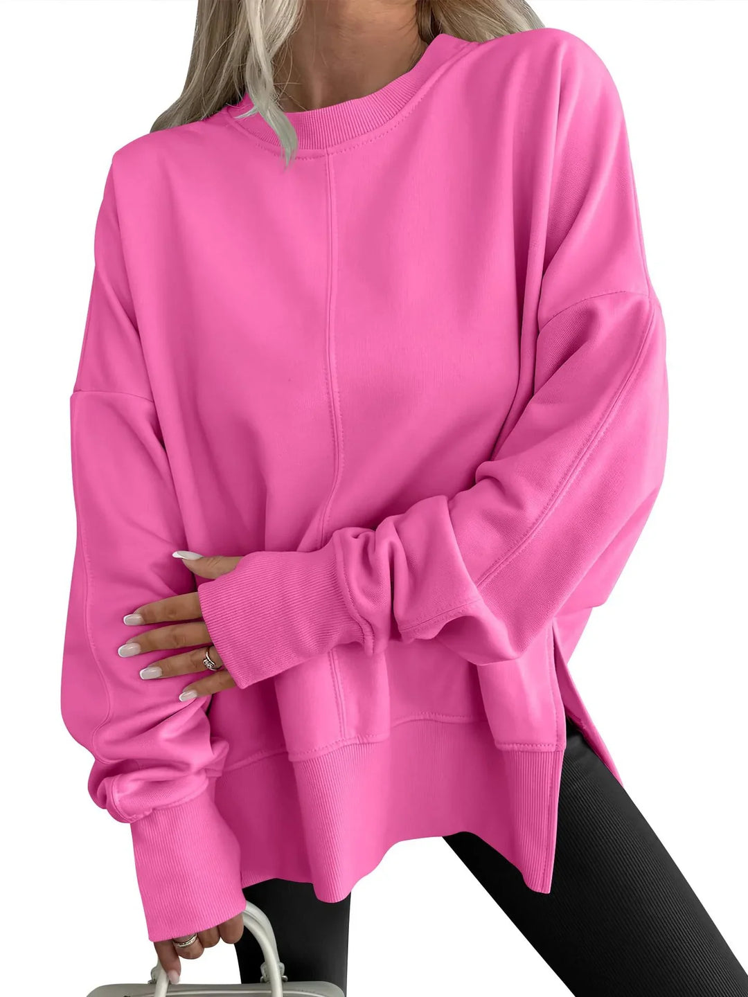 Woman wearing oversized bright pink sweatshirt paired with black pants holding white bag