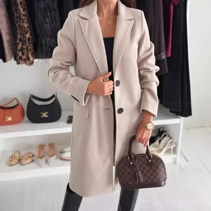 Woman wearing beige long wool coat holding brown patterned handbag in stylish clothing store