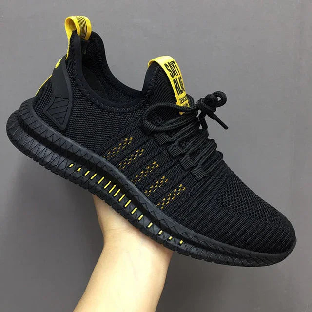 Black and yellow sports shoe with knitted upper, black sole, and yellow heel and tongue tabs held in hand