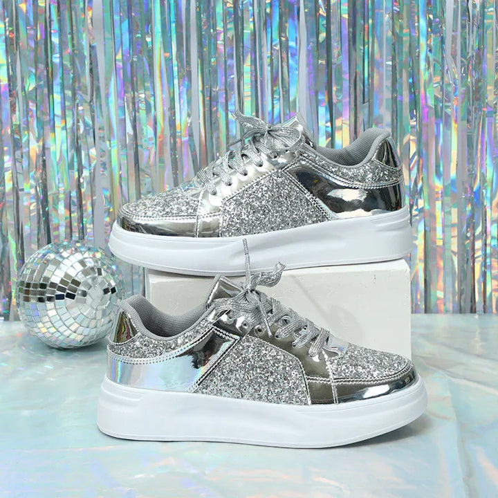 Silver glitter and metallic sneakers with white soles on white block, disco ball and holographic backdrop