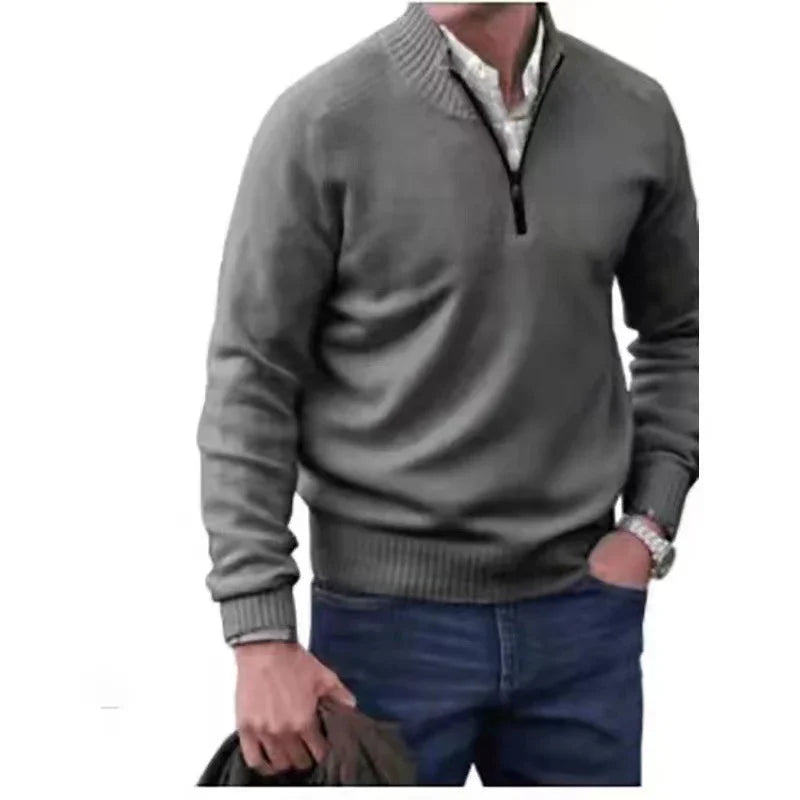 Man wearing grey quarter-zip sweater over white shirt with blue jeans holding jacket