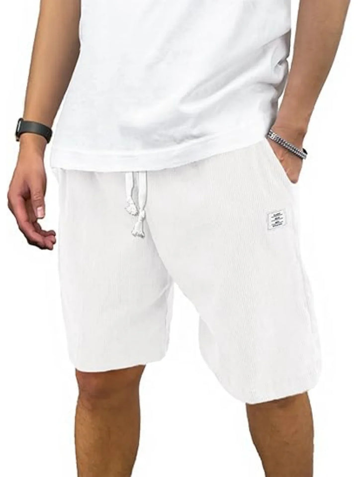 Close-up of a man wearing white casual drawstring shorts and a white shirt, accessorized with a smartwatch and bracelet