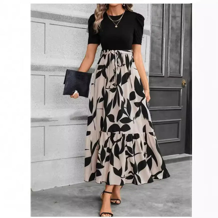 Woman wearing black puff sleeve top and beige maxi skirt with black leaf print, holding black clutch