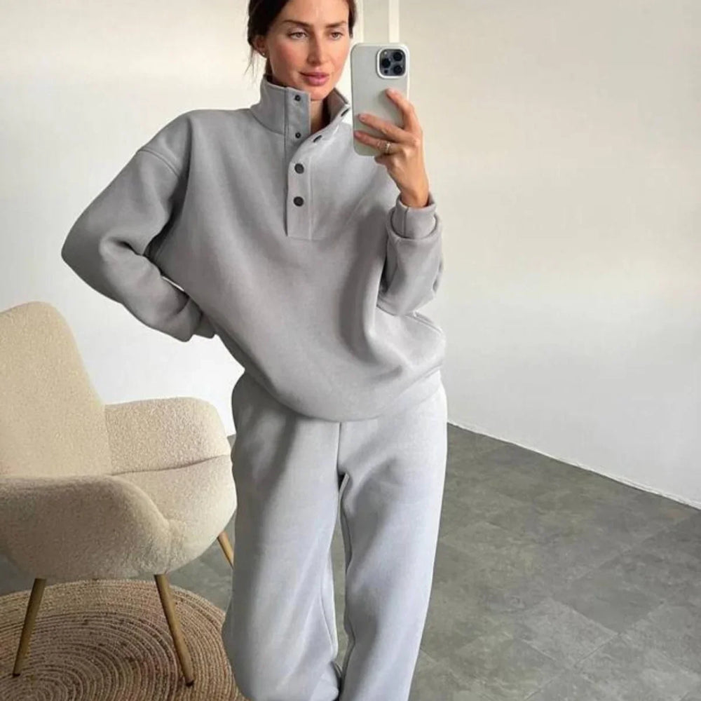 Woman wearing light gray fleece pullover and matching sweatpants taking a mirror selfie indoors