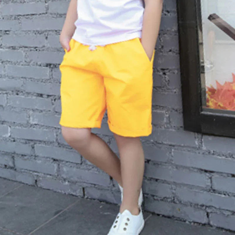 Child wearing bright yellow shorts and white sneakers standing against gray brick wall