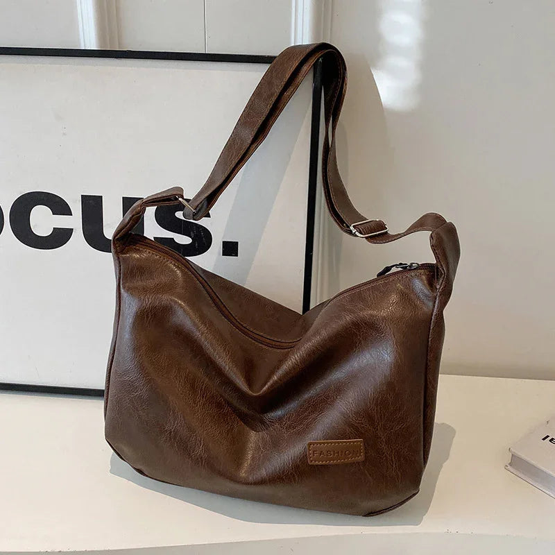 Brown leather shoulder bag with adjustable strap and embossed fashion label on white shelf