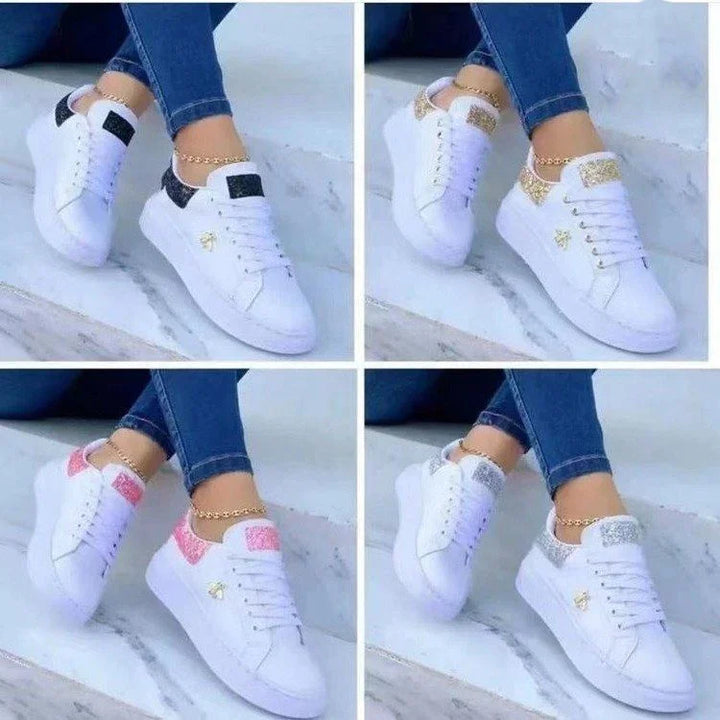 Four pairs of white sneakers with glitter accents in black, gold, pink, and silver worn with blue jeans on a marble floor