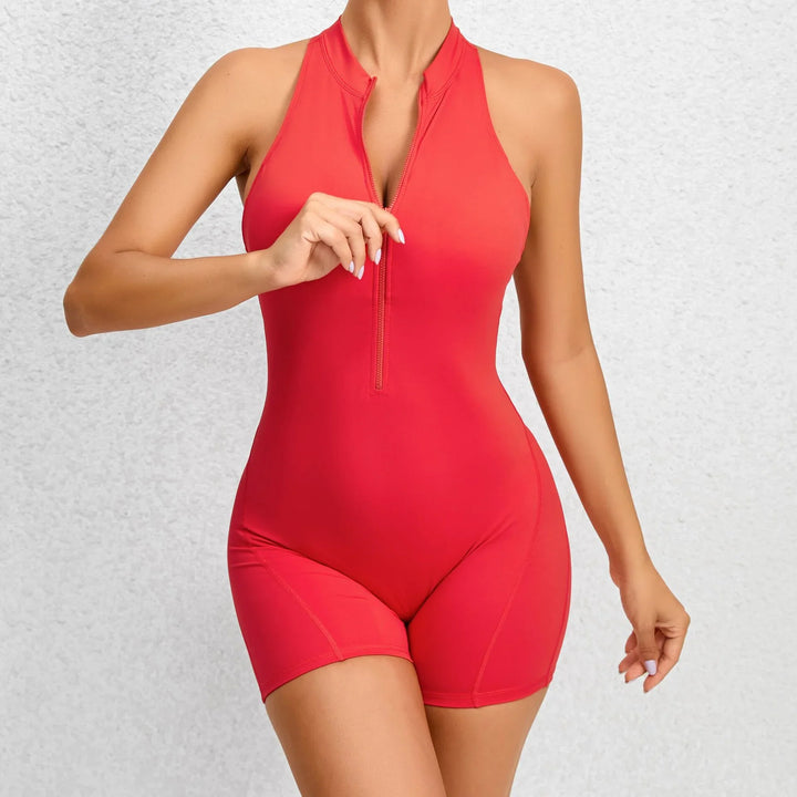 Woman wearing red sleeveless zipper front athletic romper against white wall
