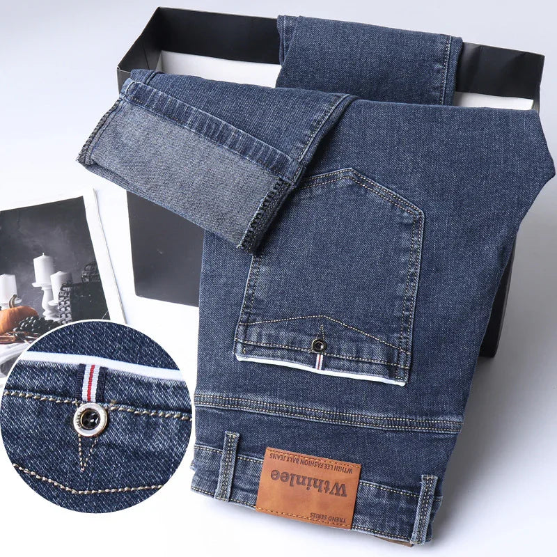 Dark blue denim jeans with folded cuffs, a back pocket with metal button, and a brown leather patch label