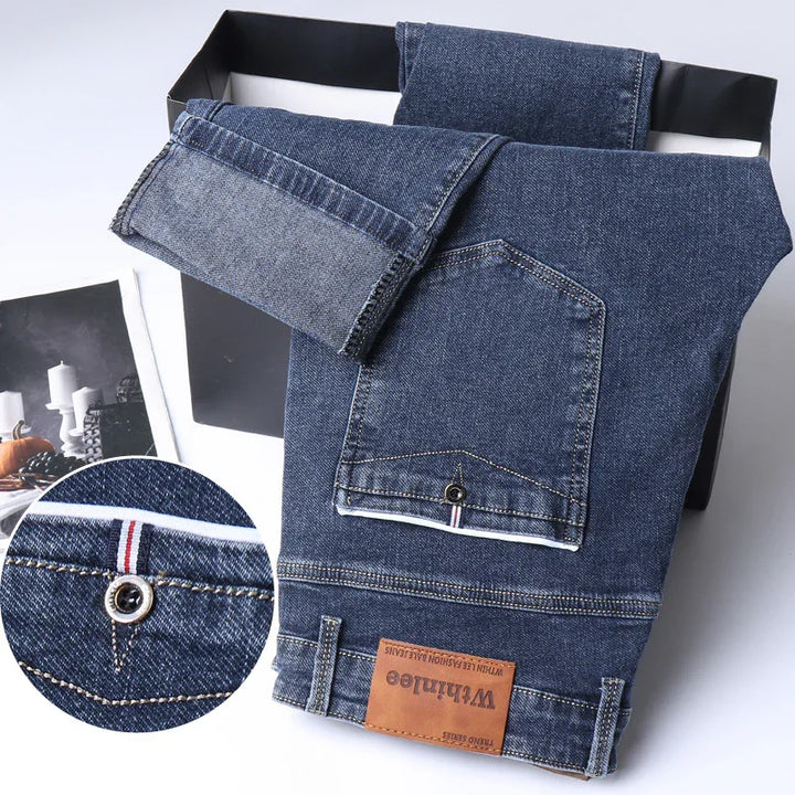 Dark blue denim jeans with folded cuffs, a back pocket with metal button, and a brown leather patch label