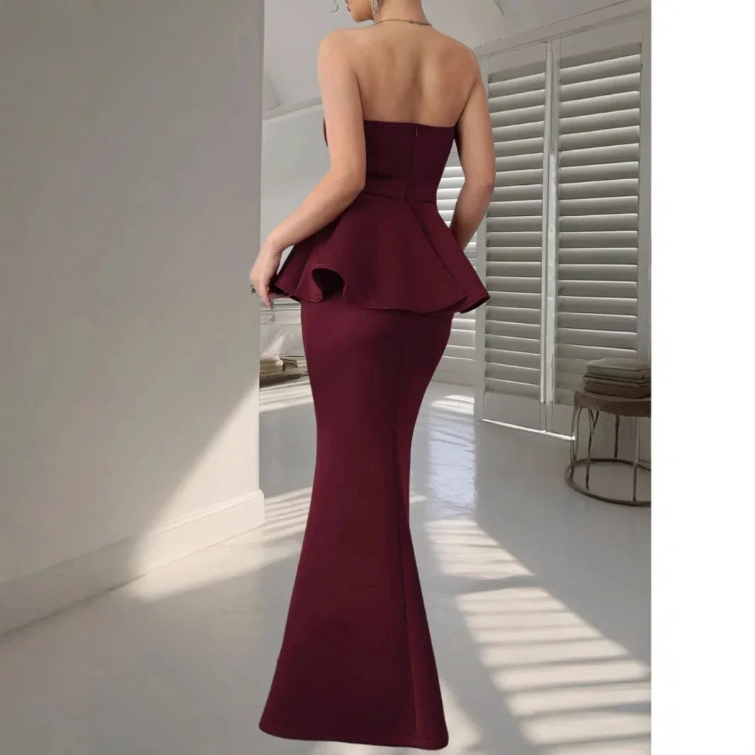 Back view of a woman wearing a strapless maroon peplum mermaid evening gown in a bright room