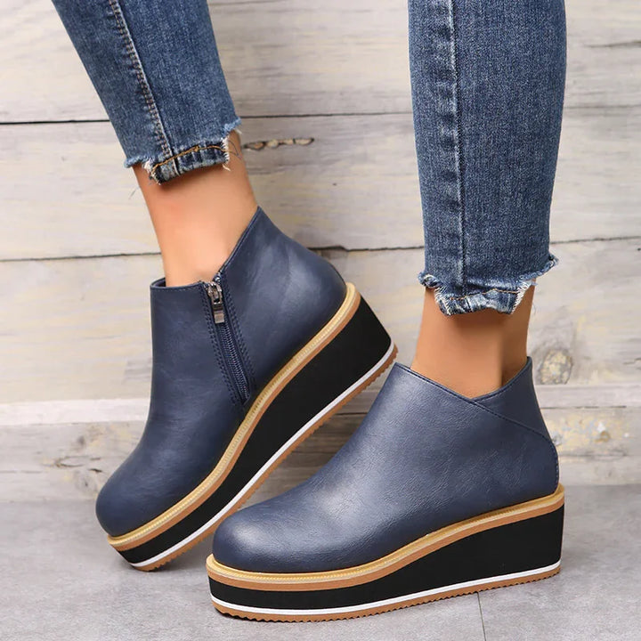 Women's navy blue leather wedge ankle boots with side zipper, worn with frayed hem jeans