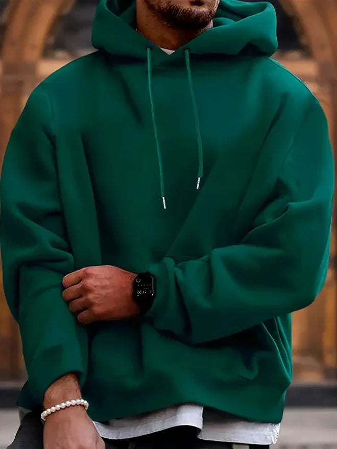 Man wearing a dark green hoodie with drawstrings, a black smartwatch, and a pearl bracelet