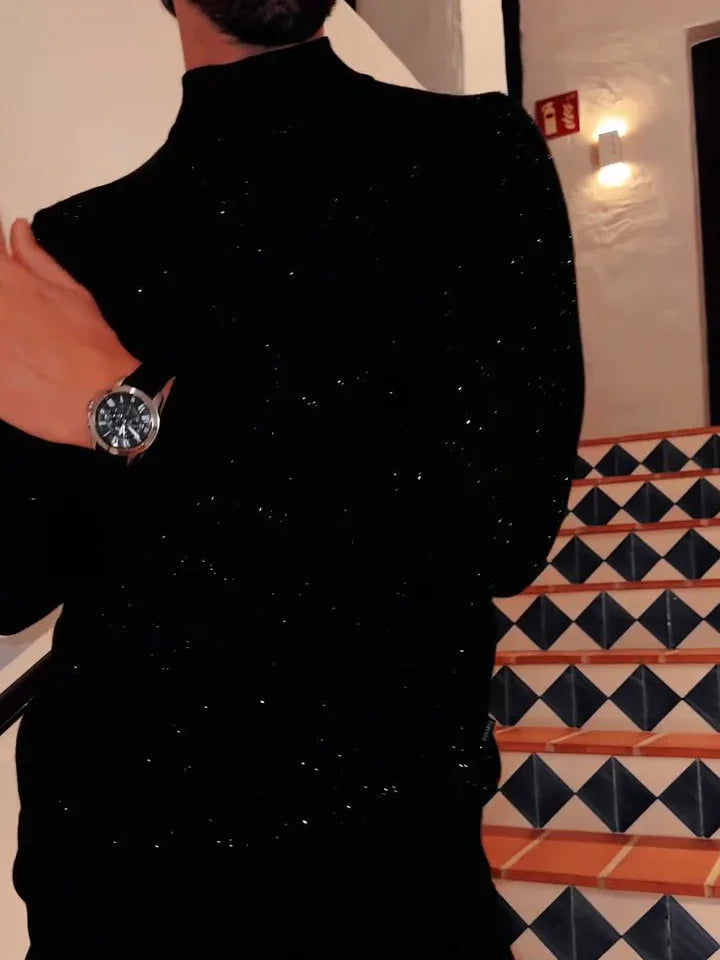 Man in black glittery sweater wearing silver watch, standing near tiled staircase with geometric pattern