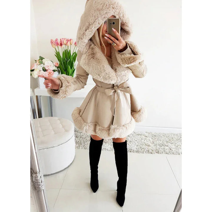 Woman wearing beige faux fur-lined coat with hood and black knee-high boots in modern indoor setting