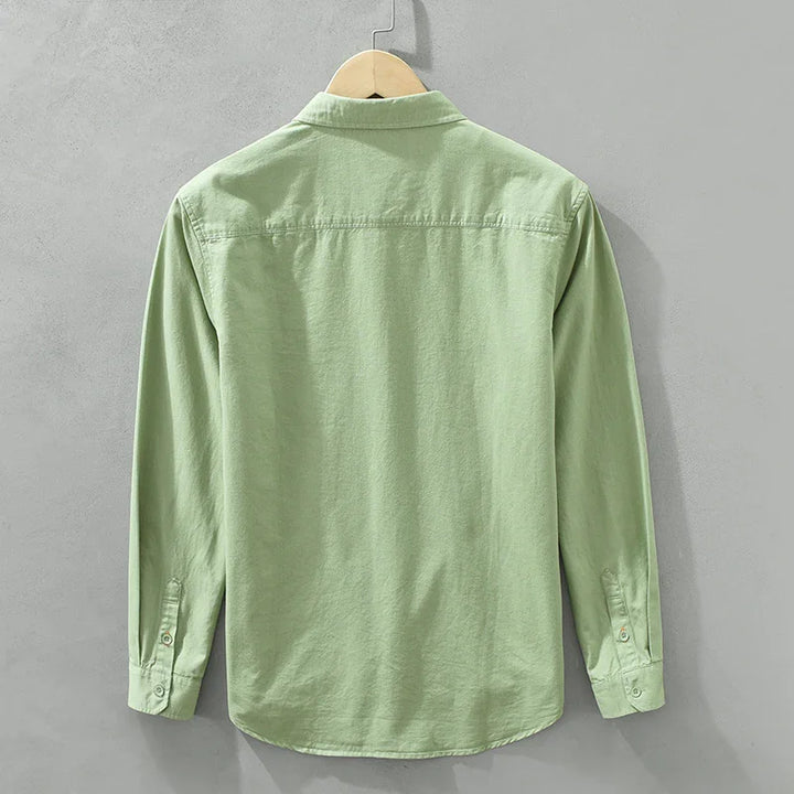 Light green long-sleeve casual shirt hanging on wooden hanger against gray wall