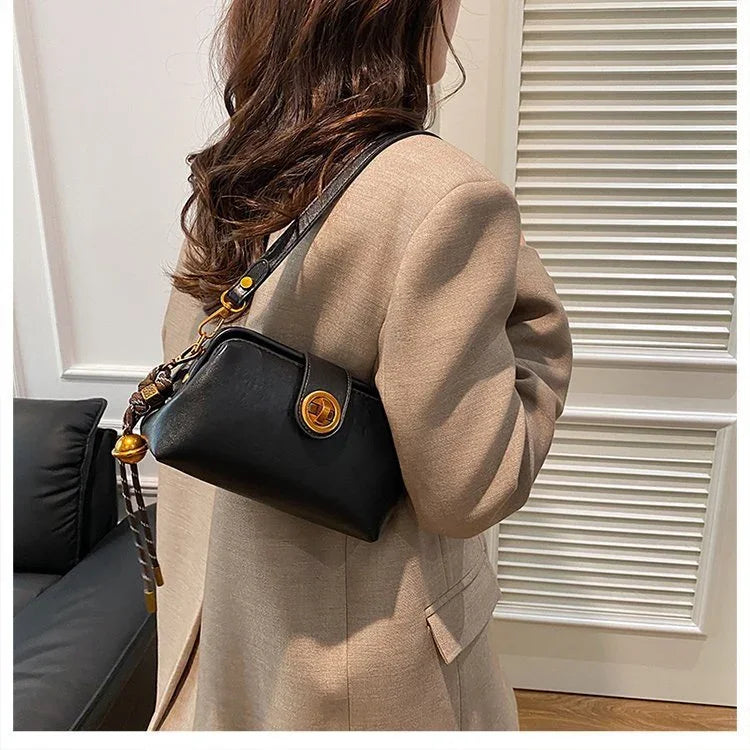 Woman wearing beige coat carrying black leather shoulder bag with gold clasp indoors
