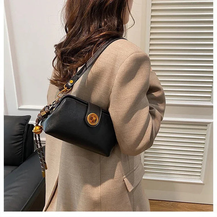 Woman wearing beige coat carrying black leather shoulder bag with gold clasp indoors