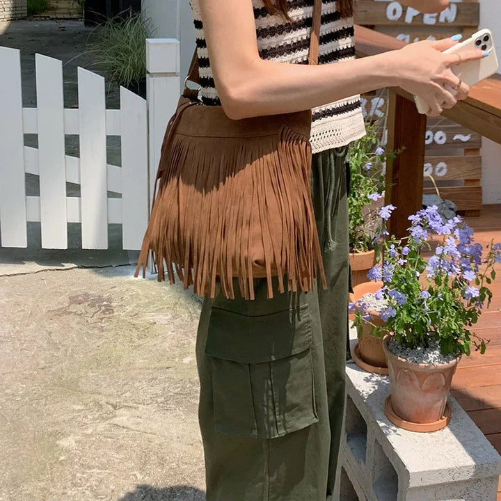 Woman wearing striped sleeveless top and olive green cargo pants holding phone with brown fringe suede bag outdoors