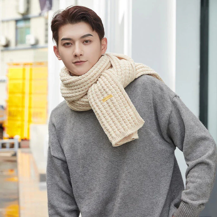 Young man wearing a beige knitted scarf and gray sweater in urban outdoor setting