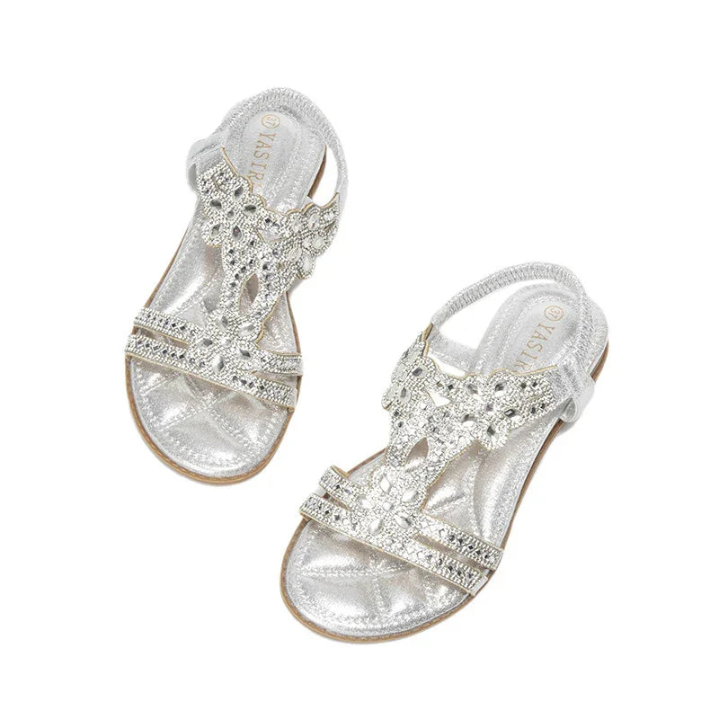 Silver flat sandals with rhinestone floral straps and ankle straps on white background