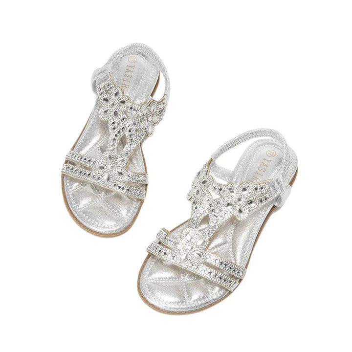 Silver flat sandals with rhinestone floral straps and ankle straps on white background