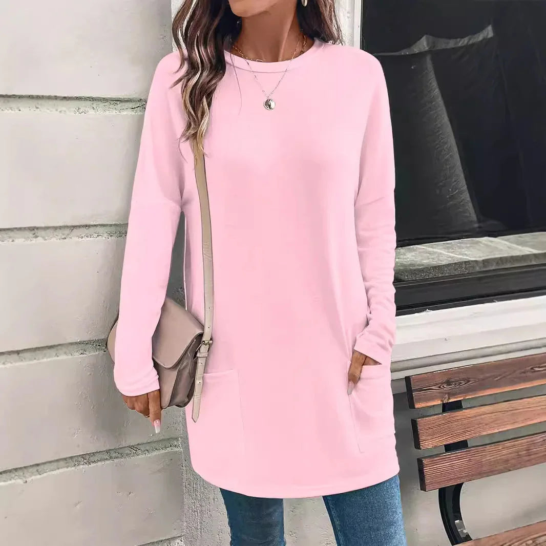 Woman wearing a light pink long-sleeve tunic sweater with front pockets, carrying beige crossbody bag