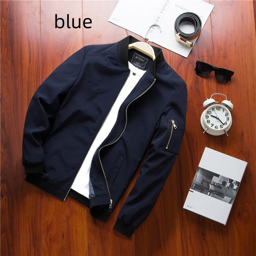Blue bomber jacket with white shirt on wooden floor, alongside sunglasses, belt, alarm clock, and book