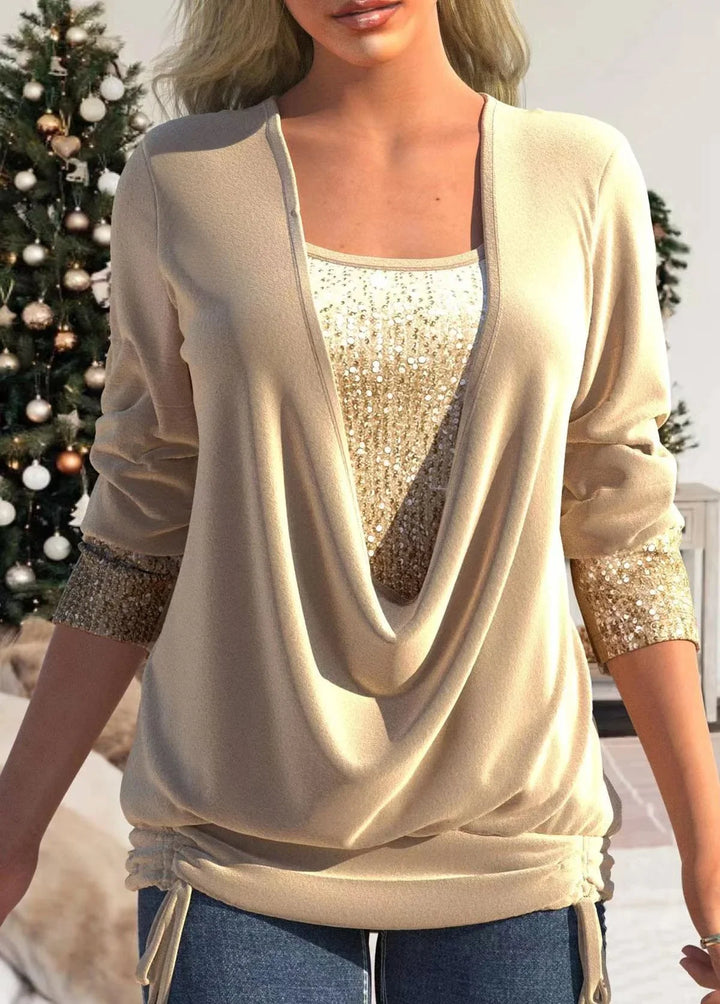 Woman wearing beige draped top with gold sequin inner layer and sleeve cuffs, standing indoors by Christmas tree