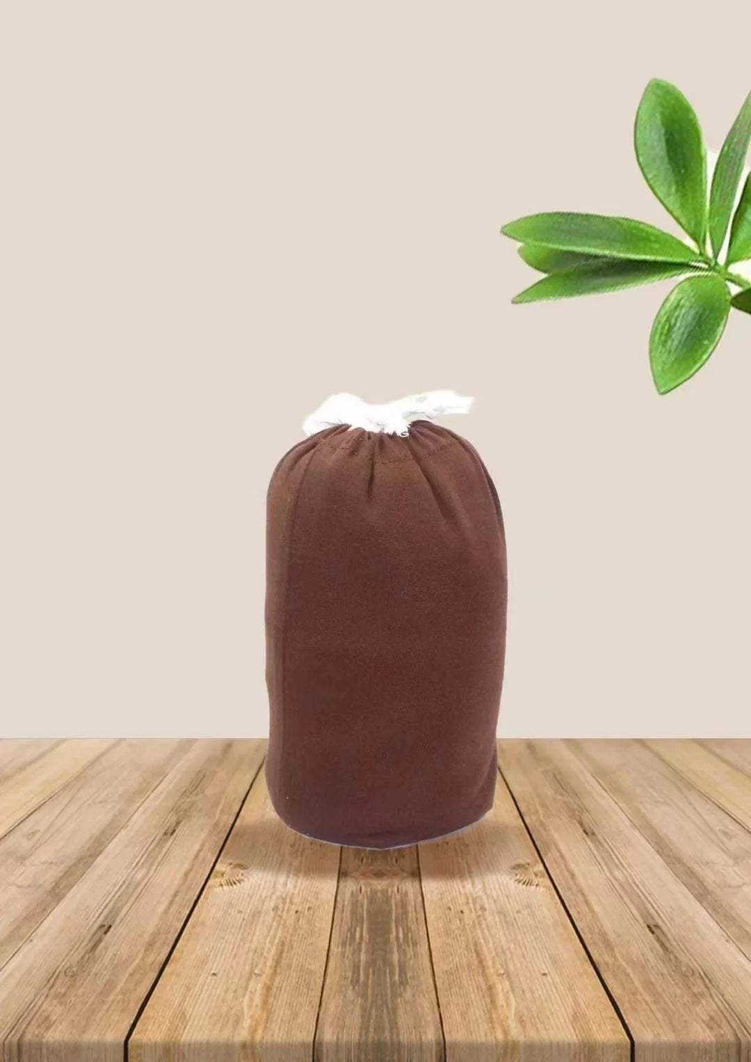 Brown drawstring bag on wooden table with green leaves background