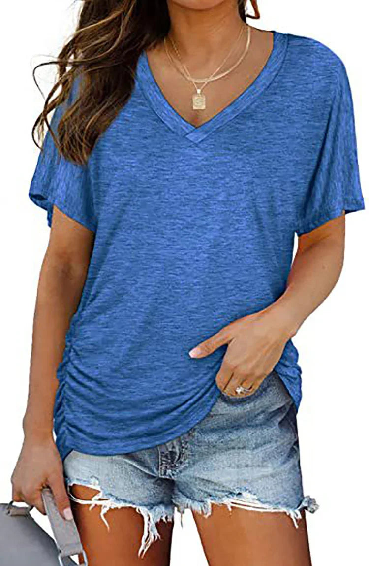 Woman wearing blue V-neck short sleeve top and distressed denim shorts holding a clutch