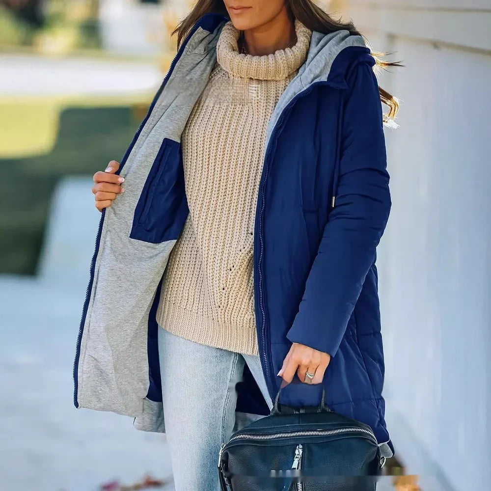 Woman wearing navy blue winter coat over beige knit turtleneck sweater and light jeans, holding black leather backpack
