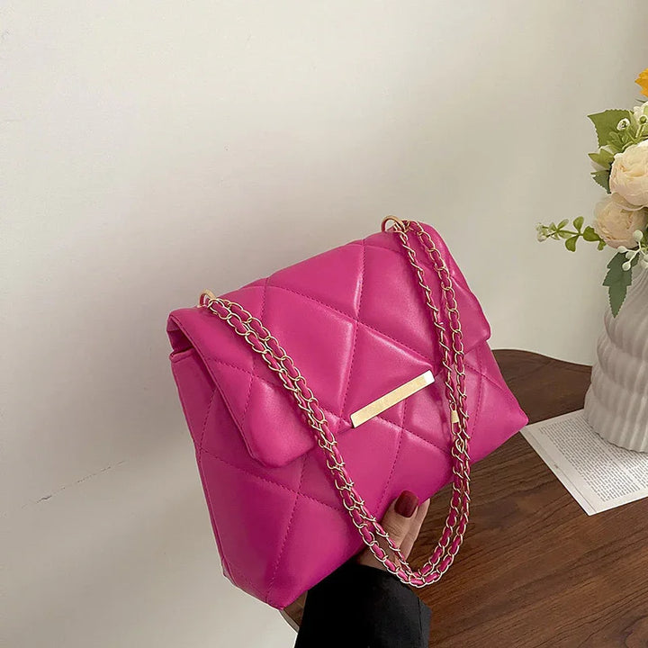 Bright pink quilted leather handbag with gold chain strap and bar detail held by hand