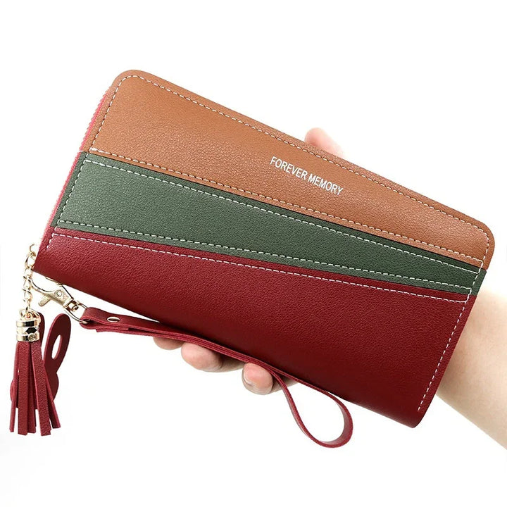 Hand holding a tri-color leather wallet in brown, green, and red with gold tassel zipper and wrist strap