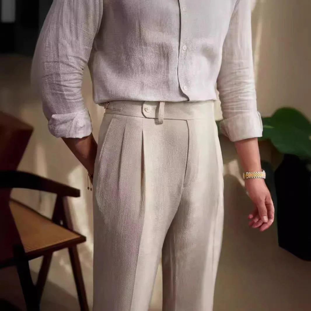 Close-up of man wearing beige pleated trousers and light linen shirt with rolled sleeves indoors