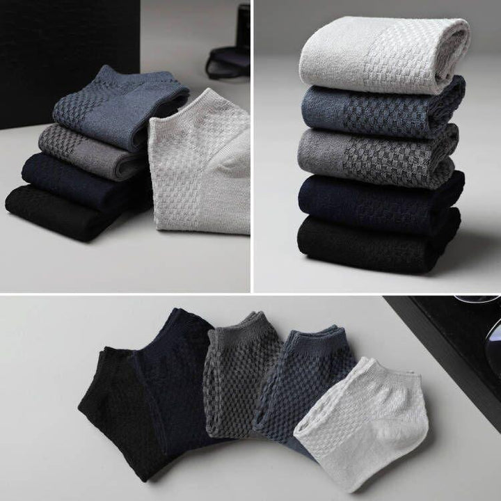 Stacked and spread men's ankle socks in black, navy, gray, and white with waffle knit pattern on gray surface