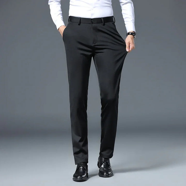Man wearing slim fit black dress pants with black belt and black shoes against gray background