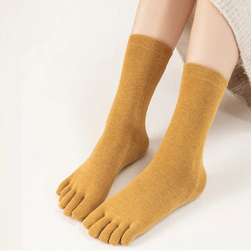 Pair of mustard yellow toe socks worn on feet with beige knit fabric background