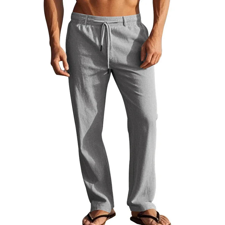 Man wearing light gray casual drawstring pants and black flip-flops on white background