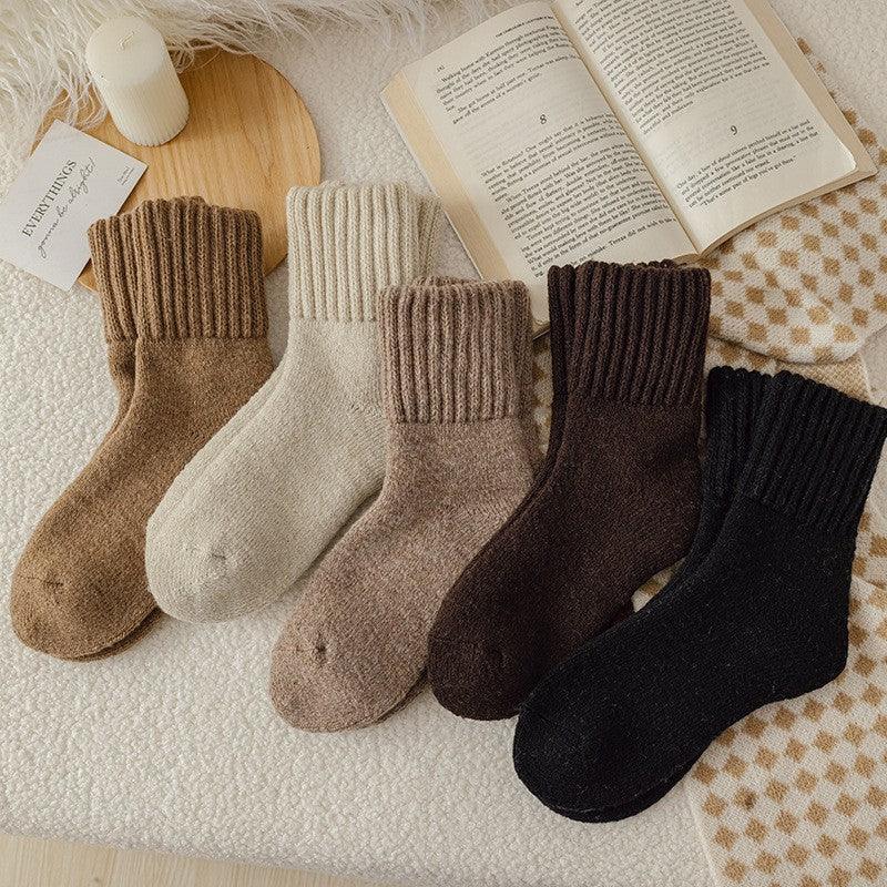 Soft wool blend socks in earth tones displayed on a cozy textured surface with an open book and candle
