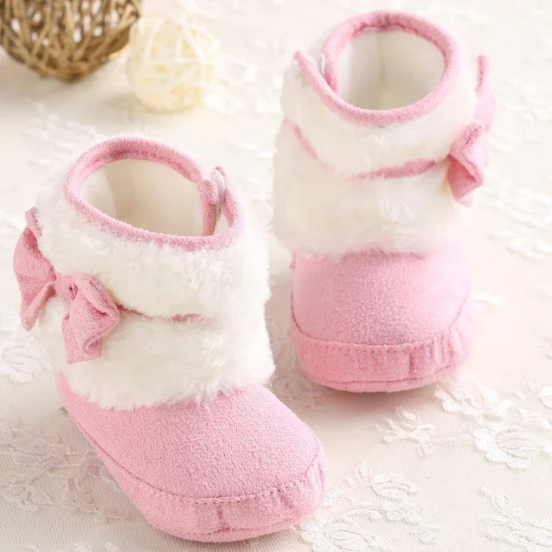 Pair of soft pink baby booties with white faux fur trim and a small bow detail