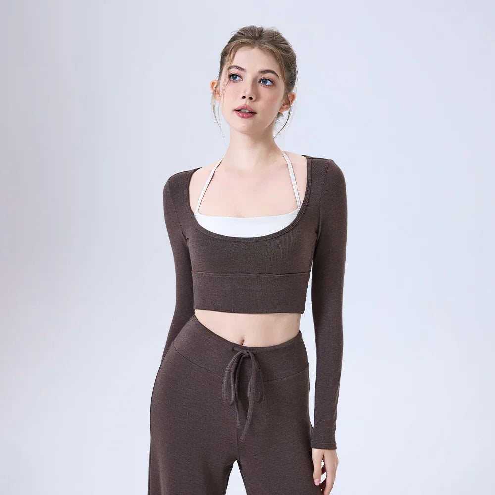 Young woman wearing brown long-sleeve crop top and matching pants with white halter top underneath