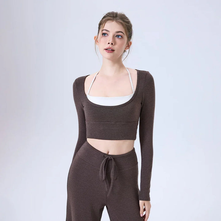 Young woman wearing brown long-sleeve crop top and matching pants with white halter top underneath