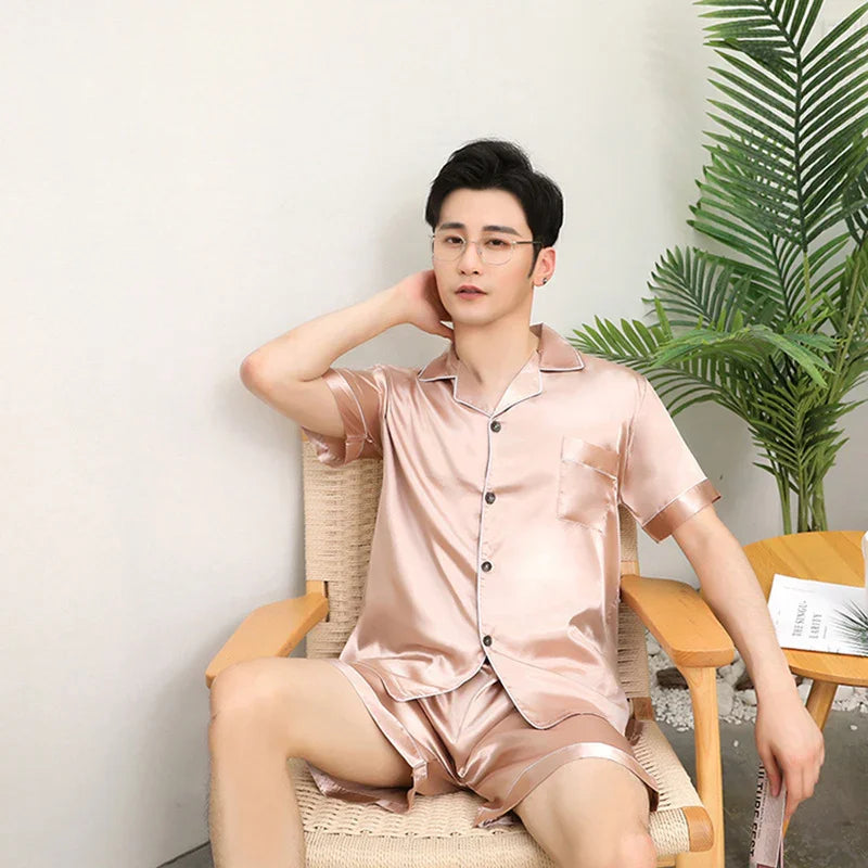 Man wearing shiny pink satin short-sleeve pajamas sitting on woven chair in modern room with green plant