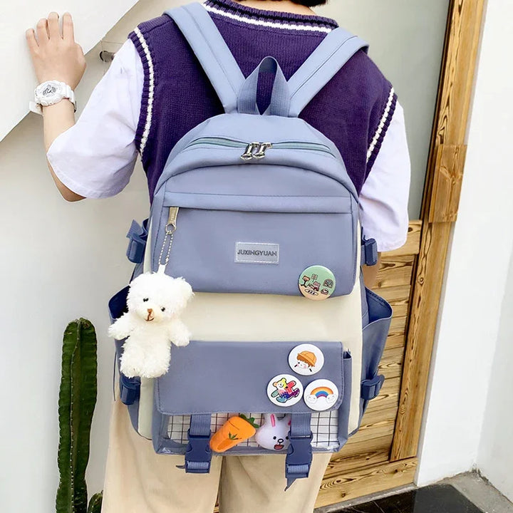 Person wearing a purple sweater vest and white t-shirt with a blue-gray Juxingyuan backpack adorned with a white teddy bear keychain and colorful pins
