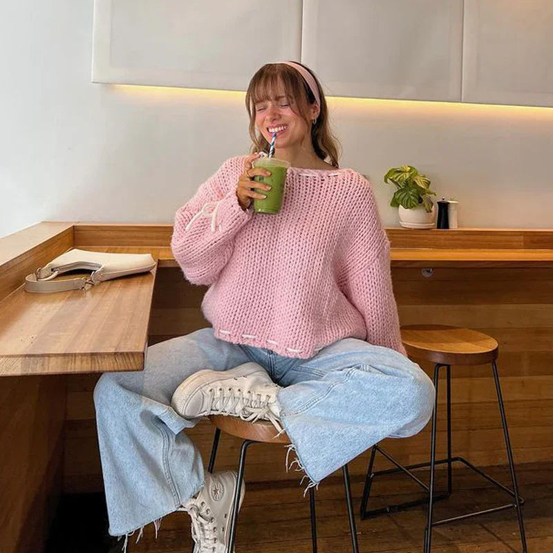 Young woman in pink knit sweater and light jeans enjoying green smoothie in modern cafe